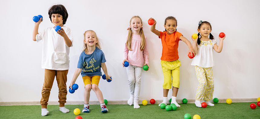 5 Kinder stehen in einer Reihe und werfen mit bunten Bällen