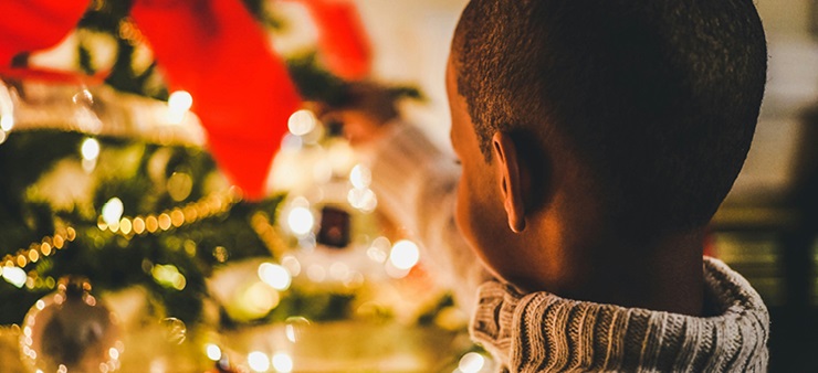 Kind steht vor leuchtendem Tannenbaum