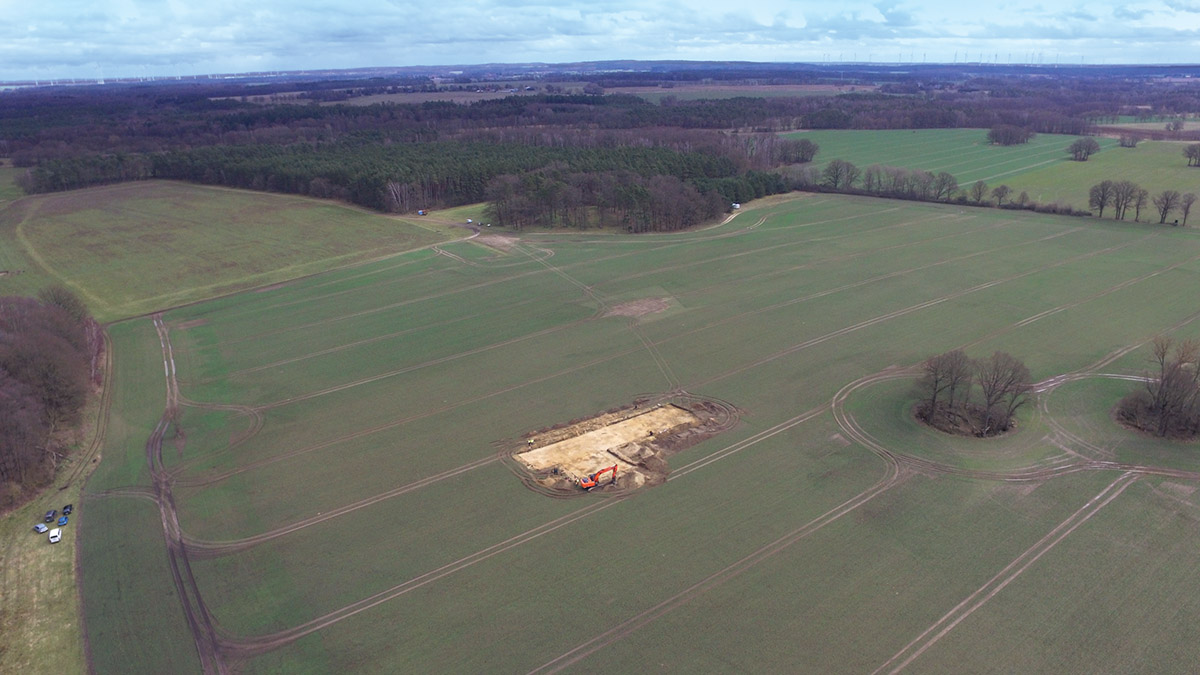 Die Grabungsfläche im März 2023 von Nordwesten während der Baggerarbeiten. Der monumentale Grabhügel wird von dem etwa 100 Jahre alten Baumbestand im Hintergrund verdeckt.