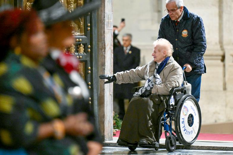 Eine ältere Frau wird im Rollstuhl durch die Heilige Pforte des Petersdoms geschoben