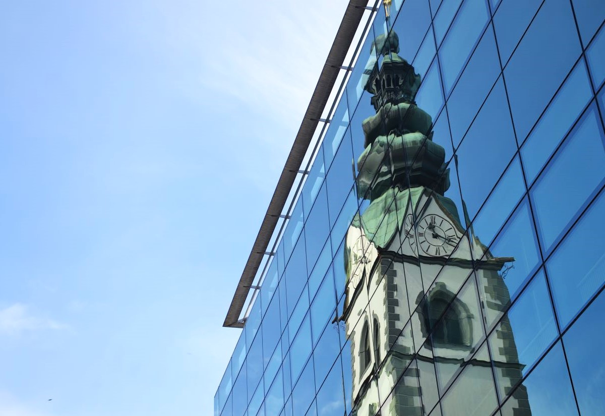 Kirchturm, der sich in einer Glasfassade spiegelt