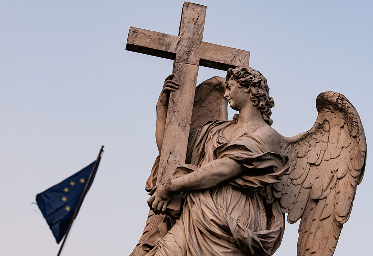 Die Statue eines Engels mit einem Kreuz auf der Ponte Sant'Angelo, der Engelsbrücke, am 7. April 2020 in Rom. Hinter der Engelsstatue weht eine Europa-Flagge im Wind.