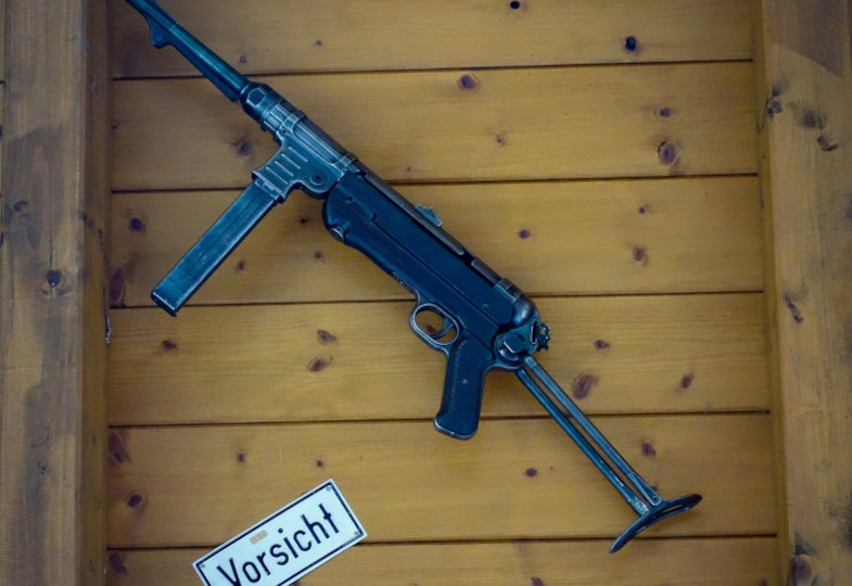 Maschinengewehr in Kiste mit Schild "Vorsicht"