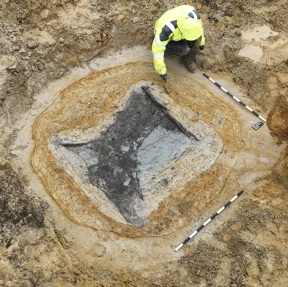 In der großen runden Baugrube zeichnet sich oben rechts, am Rande der dunklen Verfüllung im Holzbrunnen, eine erste Bohle des Brunnenkastens ab. 