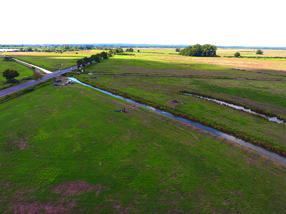 Hunte. Fluchtstangen zu beiden Seiten des Hunte-Kanals markieren eine bei älteren Grabungen freigelegte Palisade. Nahe der Straße, außerhalb der ­Palisade, wurden im Sommer 2022 ­weitere Spuren der Moorsiedlung entdeckt.