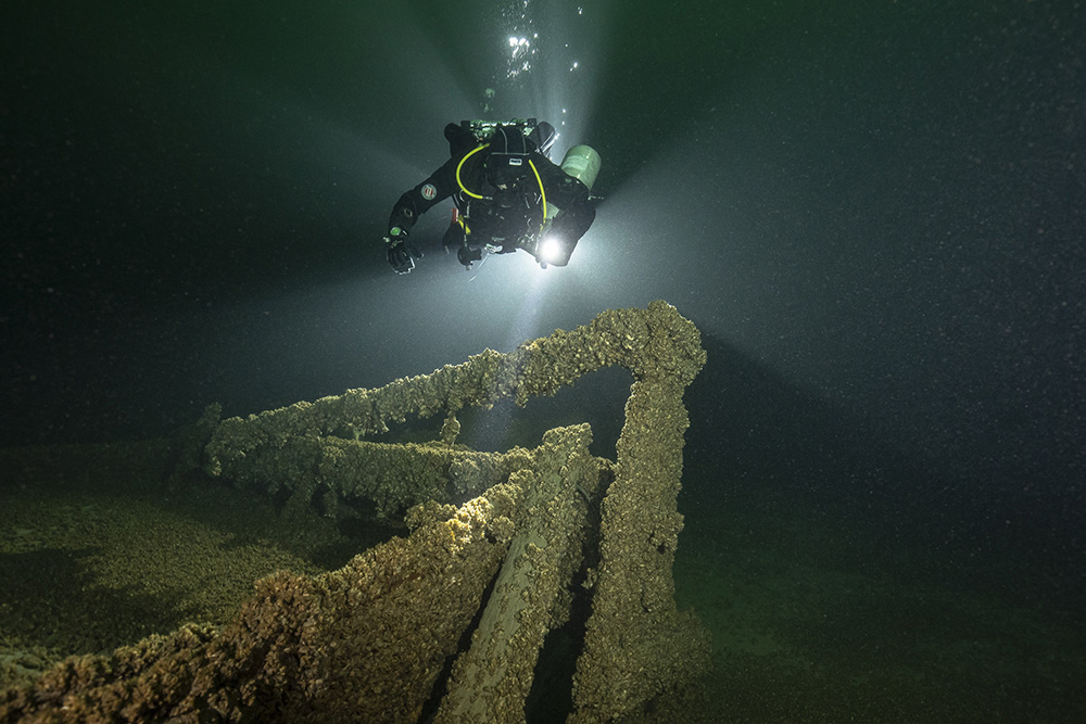 Eine Forschungstaucherin taucht ein mit Quaggamuscheln bewachsenes Wrack im Bodensee an, um dieses zu dokumentieren.